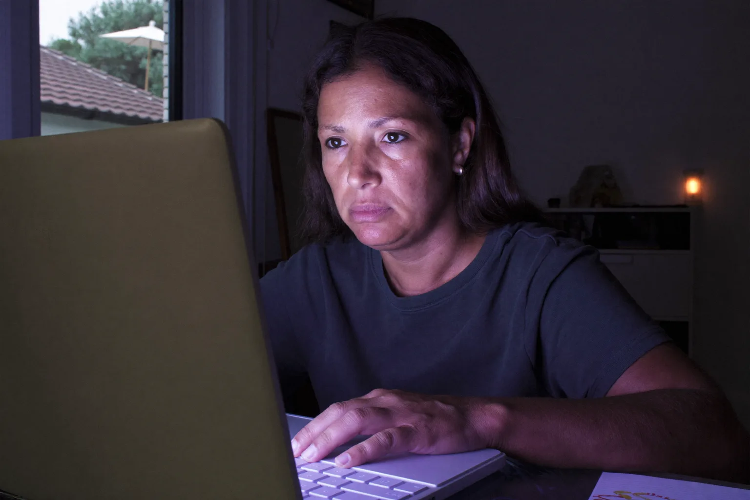Una persona asseguda a l’escriptori de casa a última hora del vespre, amb la mirada perduda més enllà de la pantalla de l’ordinador portàtil i les mans encara al teclat, mostrant l’esgotament aplanat del burnout a la feina
