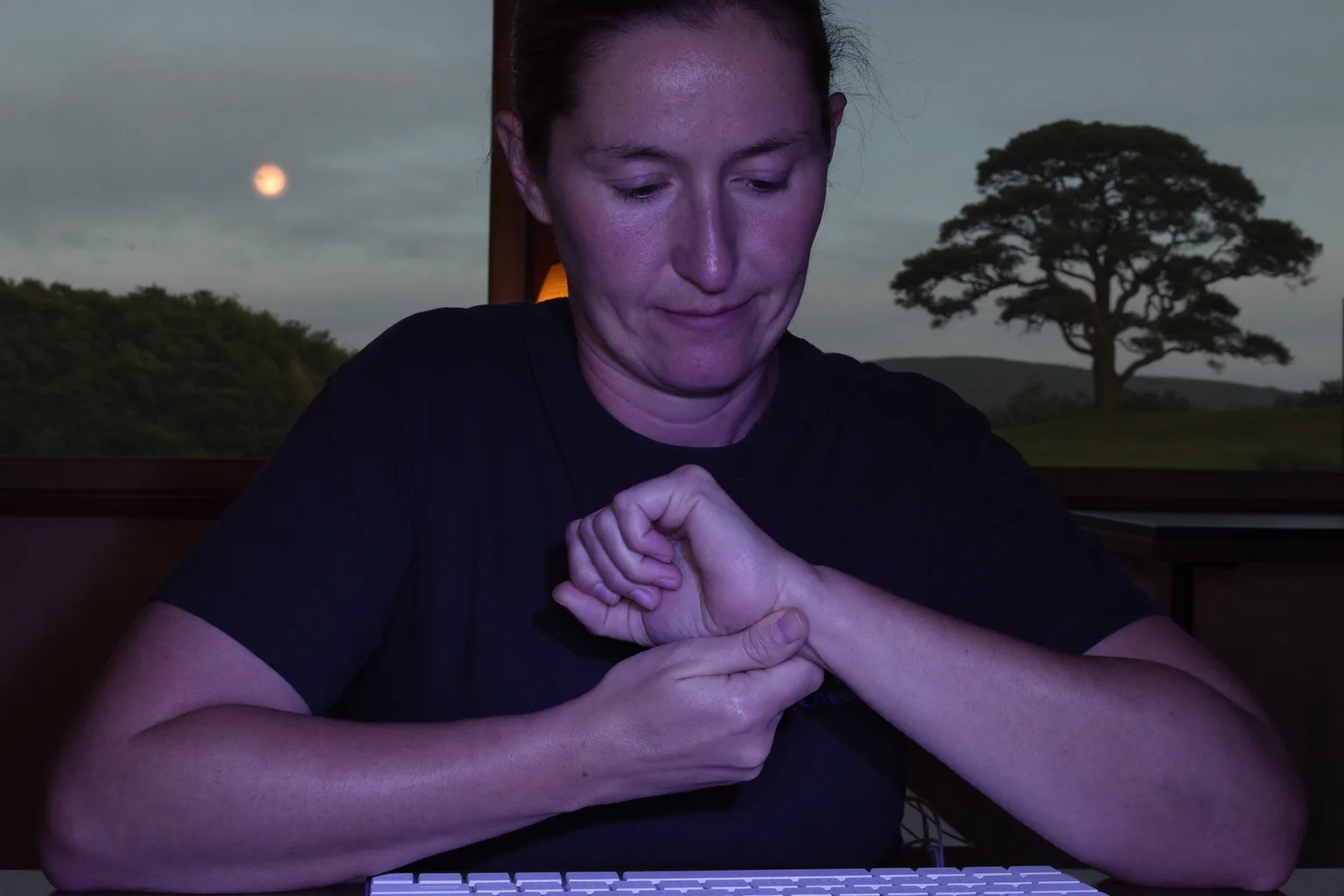 A person at a desk holding their right wrist with the other hand, keyboard in front of them, showing the numb, aching hand of carpal tunnel symptoms