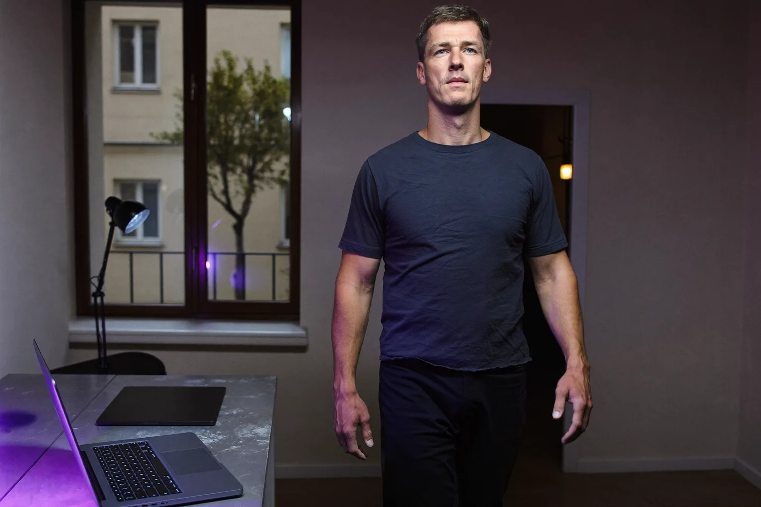 Zavřený notebook na domácím stole večer, rozsvícené světlo v místnosti a člověk odcházející pryč, symbol konce pracovního dne na home office