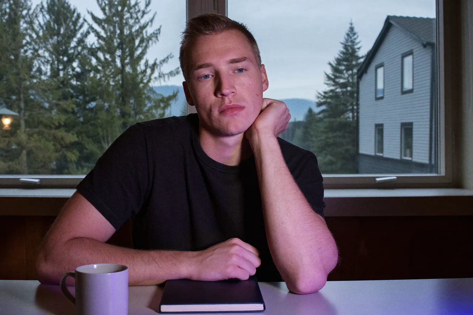En studerende ved et skrivebord sent på aftenen, hagen hvilende i den ene åbne håndflade, ansigtet lyst op fra siden af skærmens skær, blikket drevet væk fra arbejdet og ud af billedet