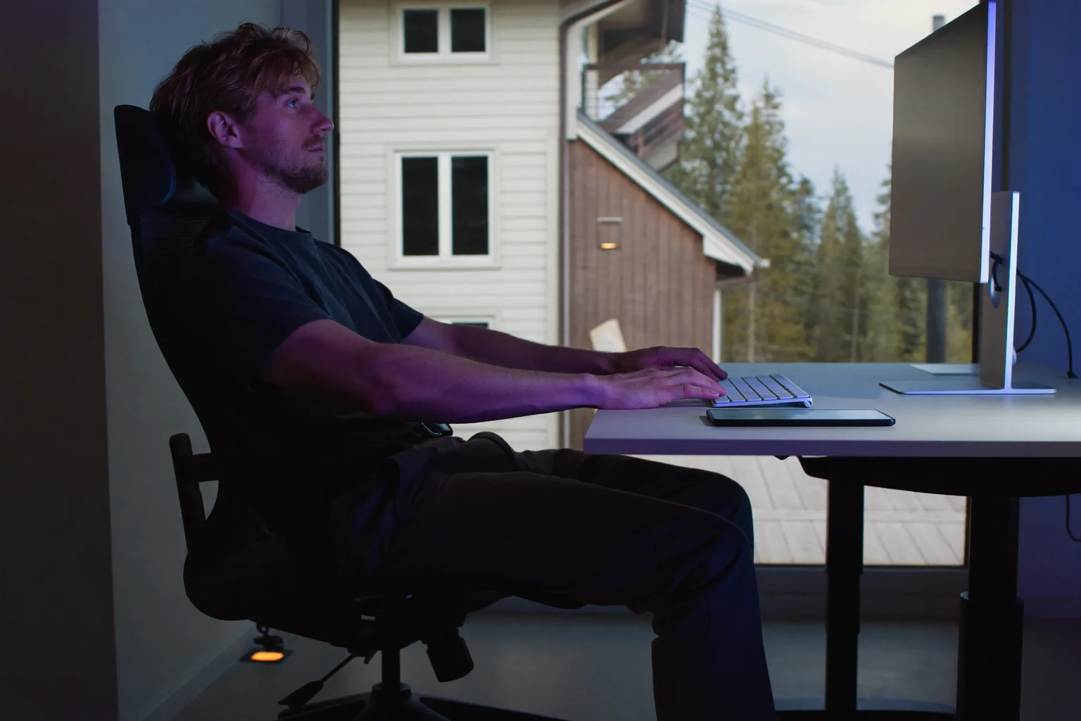 En person set fra siden, sidder ved et skrivebord med fødderne fladt på gulvet, ryggen mod stolens støtte, underarmene i niveau med skrivebordet og skærmen i øjenhøjde, den ideelle kontorholdning