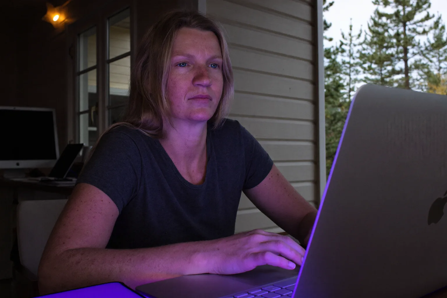 En person, der sidder ved et hjemmekontor sent om aftenen og stirrer forbi laptopskærmen med hænderne stadig på tastaturet, et billede på den flade udmattelse ved udbrændthed på arbejdet