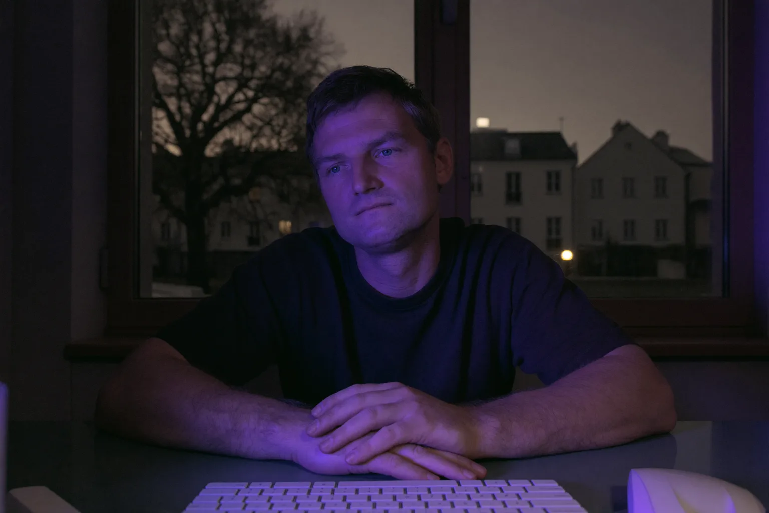 Eine Person sitzt spätabends am Schreibtisch zuhause und blickt am Laptop-Bildschirm vorbei, die Hände noch auf der Tastatur: der stumpfe Ausdruck von Burnout im Job