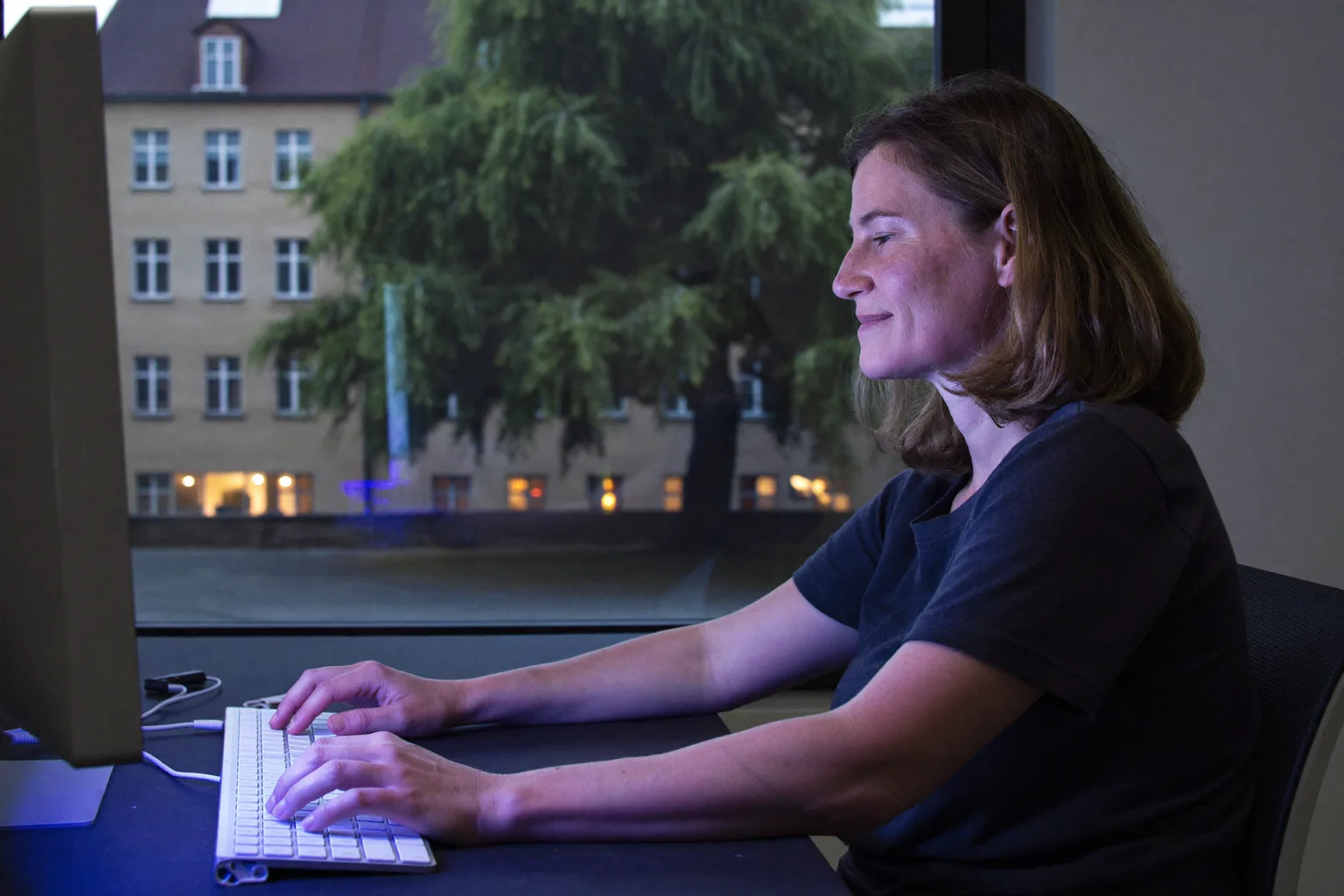 Eine Person von der Seite an einem Schreibtisch: Füße flach auf dem Boden, Rücken an der Rückenlehne, Unterarme auf Höhe des Schreibtisches und der Monitor auf Augenhöhe, die Referenzhaltung am Schreibtisch