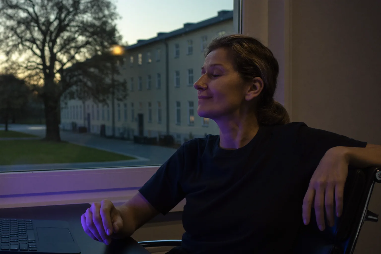 Eine Person im Homeoffice, die am Schreibtisch innehält und für die Konzentration aus dem Fenster schaut, weg vom Laptop