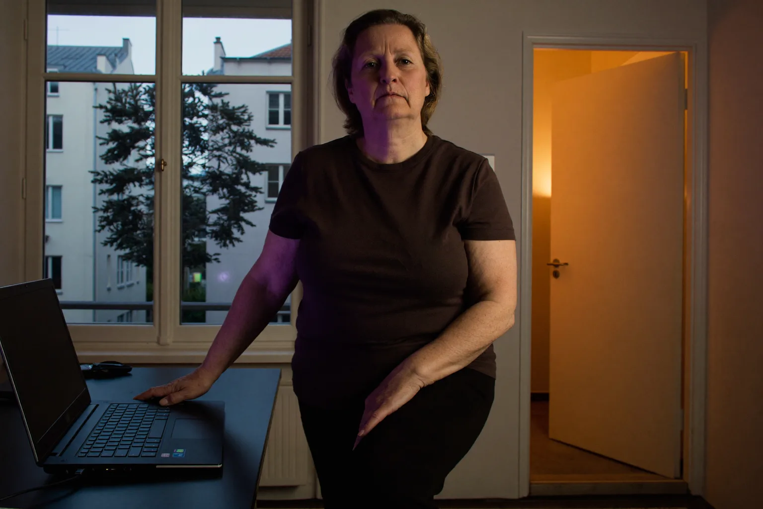 Ein zugeklappter Laptop auf einem Schreibtisch zuhause am Abend, mit eingeschaltetem Licht im Raum und einer Person, die weggeht, als Symbol für das Ende eines Homeoffice-Arbeitstags