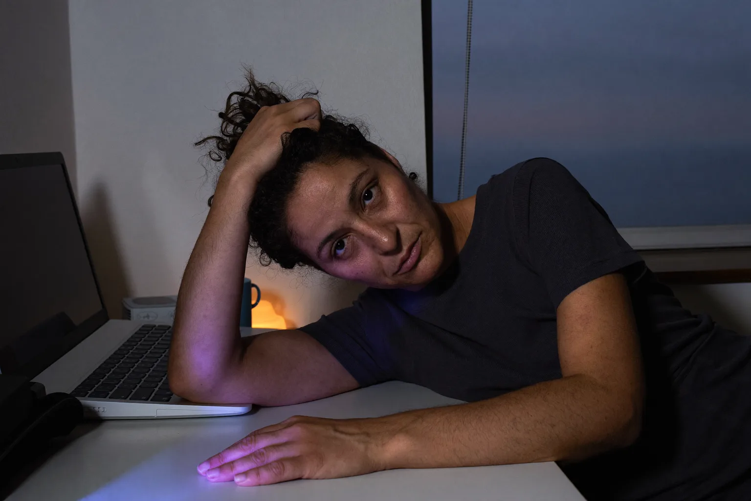 Ένα άτομο σε γραφείο στο σπίτι αργά το βράδυ, με το κεφάλι γερμένο σε ένα χέρι και τα δάχτυλα μέσα στα μαλλιά του, με το βλέμμα χαμηλωμένο και θολό, με το άλλο αντιβράχιο ακίνητο πάνω σε ένα άδειο γραφείο