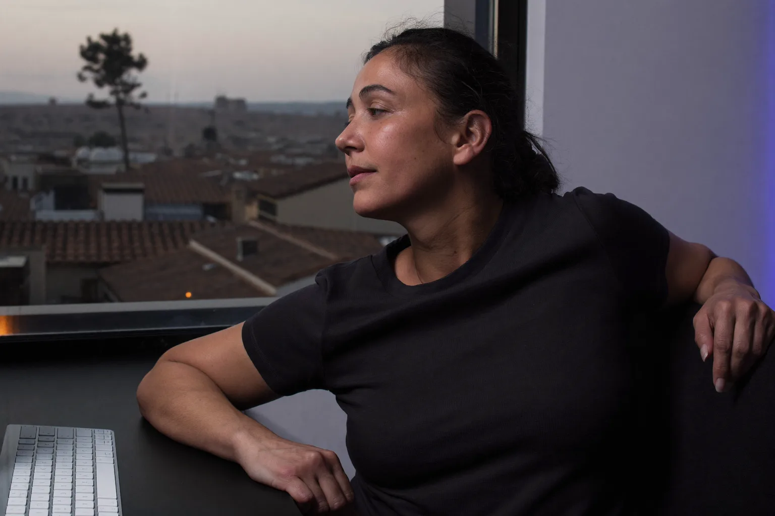 Una persona que teletrabaja haciendo una pausa en su escritorio para mirar por la ventana, lejos del portátil