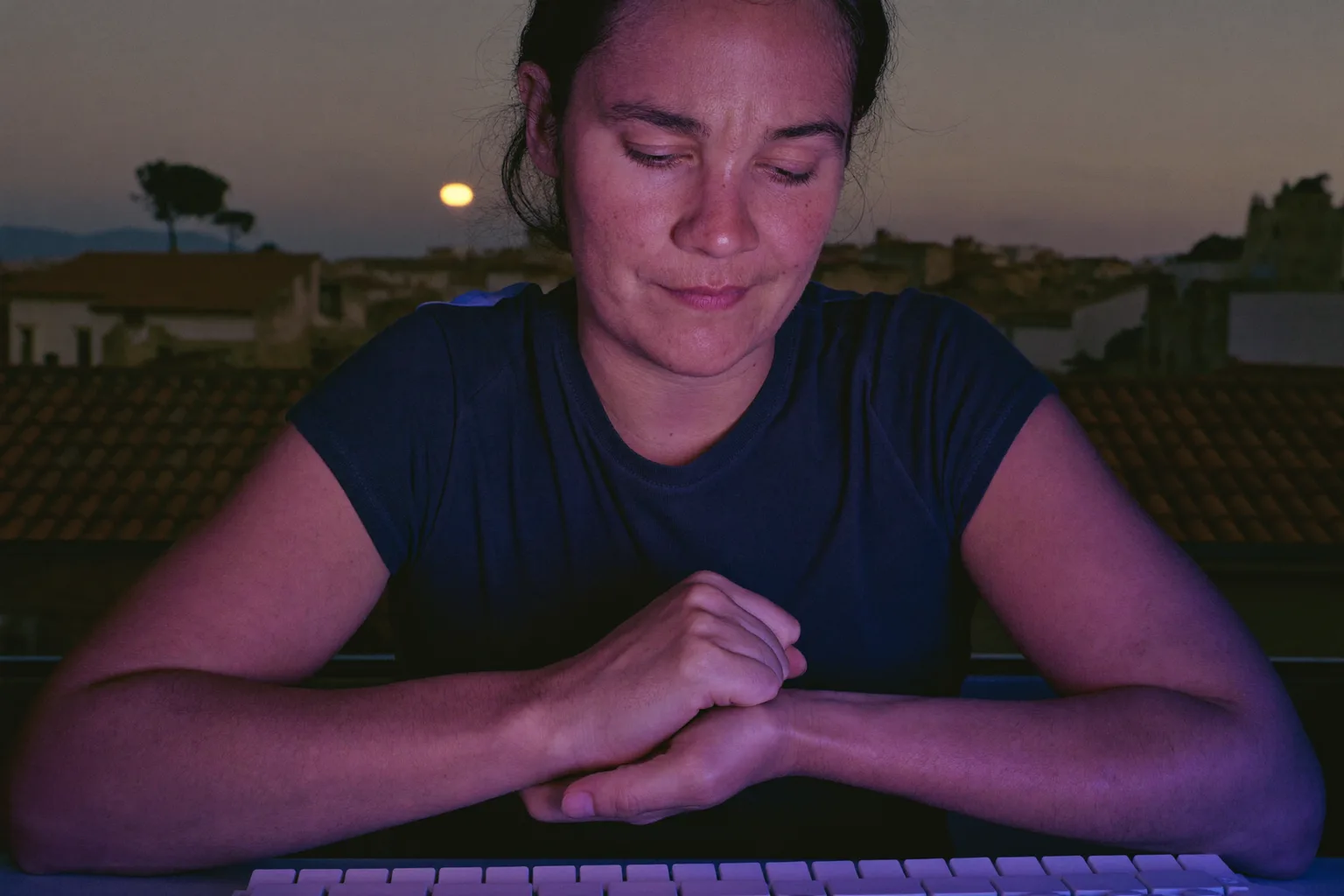 Una persona en su escritorio sujetándose la muñeca derecha con la otra mano, con el teclado delante, mostrando la mano dolorida y dormida propia de los síntomas del túnel carpiano