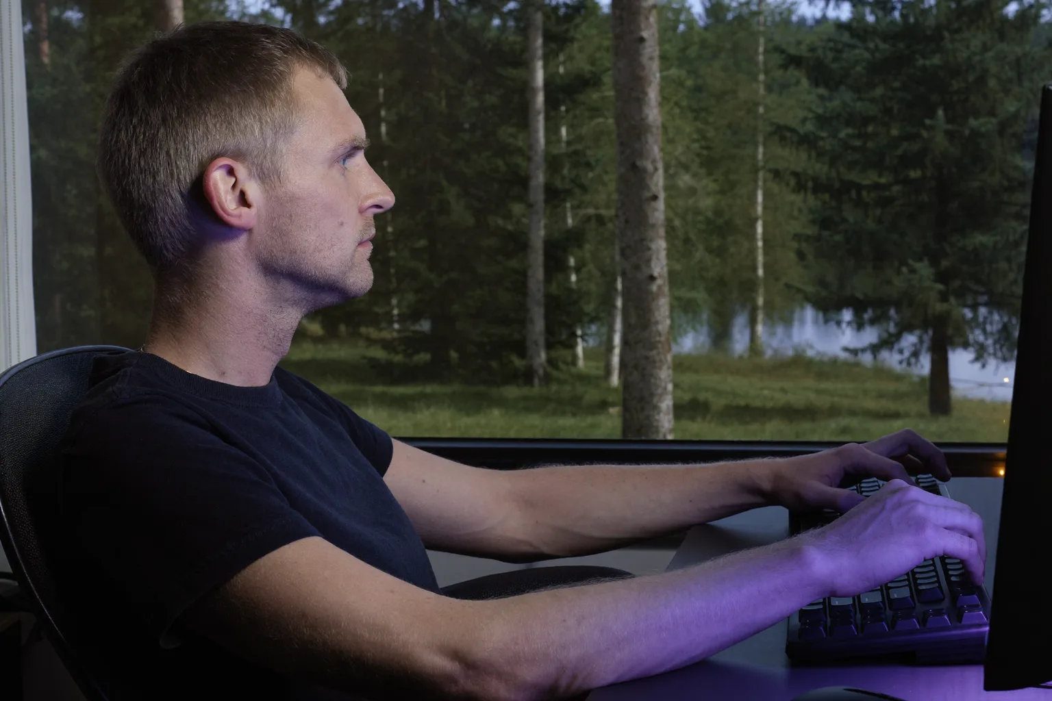 Sivulta kuvattu henkilö istumassa työpöydällä jalat tasaisesti lattialla, selkä tuolin tukea vasten, kyynärvarret pöydän tasolla ja näyttö silmien korkeudella: oikea työpisteasento