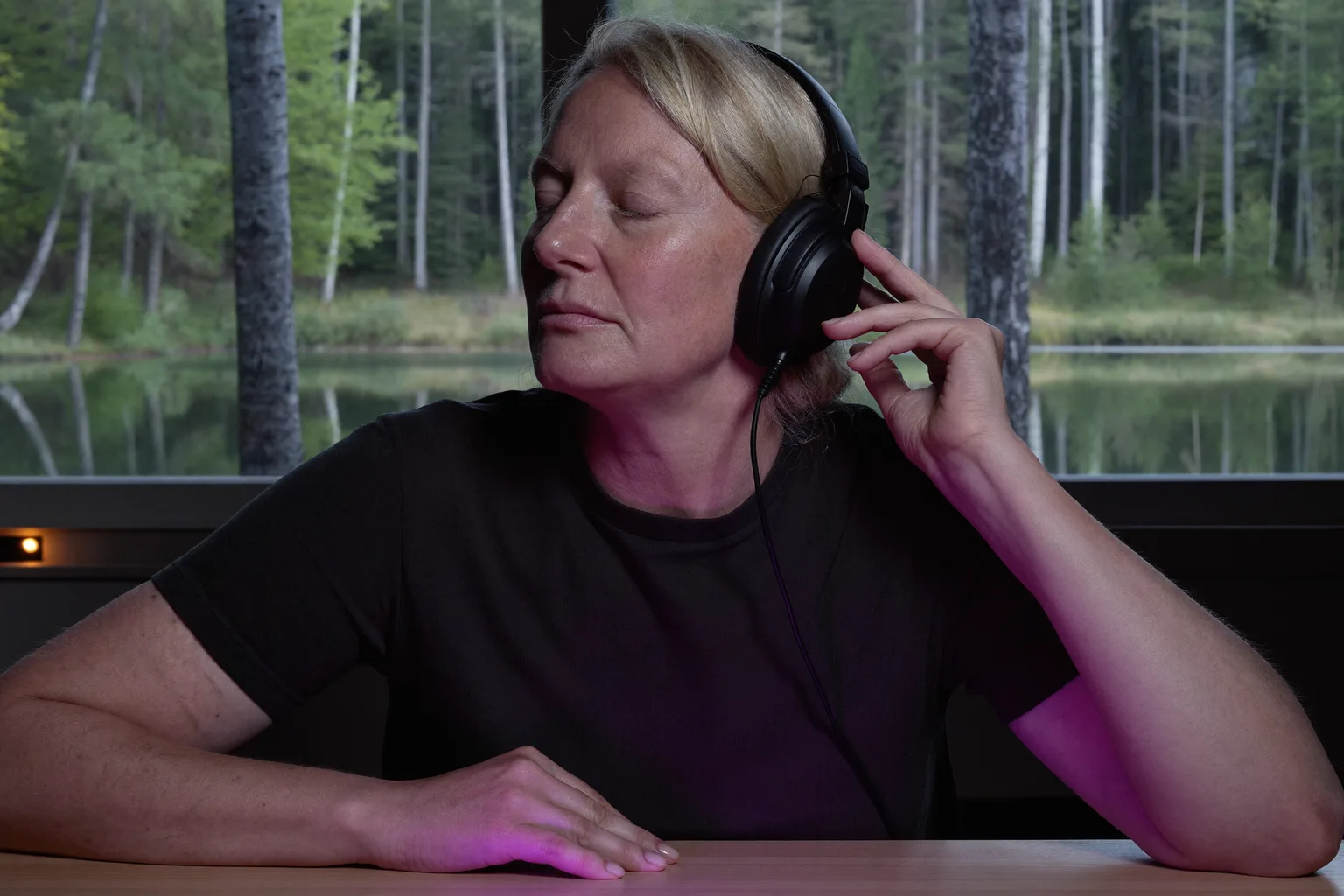 Henkilö työpöydän ääressä isot kuulokkeet päässä, silmät kiinni ja toinen käsi kuulokkeen kupua vasten, syvällä työrupeamassa musiikin soidessa