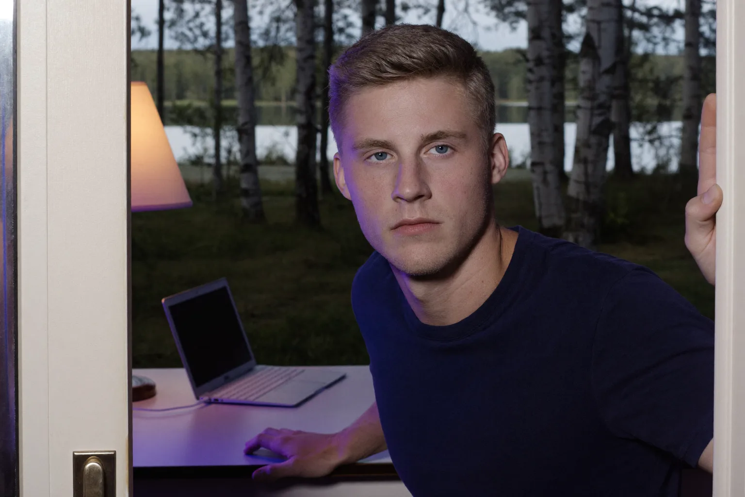 Suljettu kannettava kotitoimiston pöydällä illalla, huoneen valo päällä ja henkilö kävelemässä pois, kuvastaen etätyöpäivän päättymistä