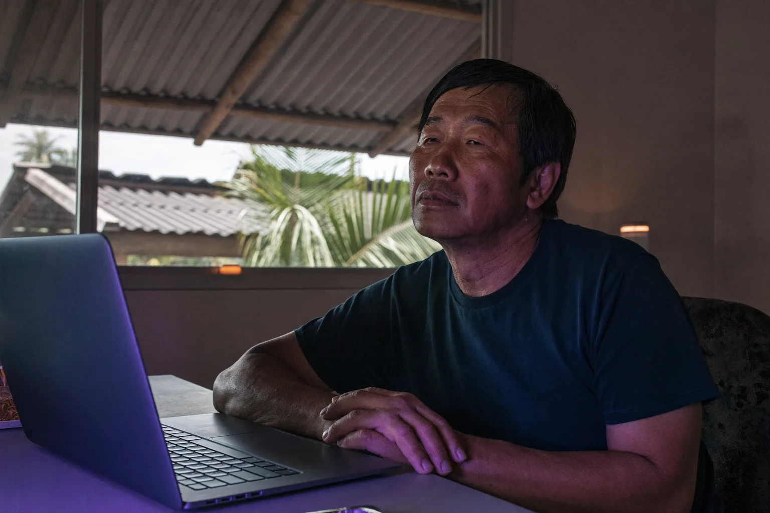 Isang remote worker na huminto sandali sa kanyang home desk para tumingin sa labas ng bintana, malayo sa laptop
