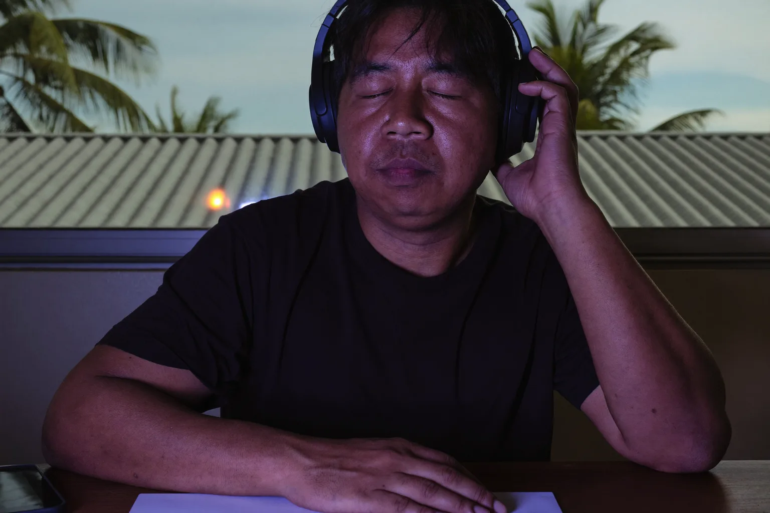 Isang tao sa harap ng desk, naka-over-ear headphones, nakapikit ang mata at may isang kamay na nakapatong sa ear cup, malalim sa isang work session habang tumutugtog ang music
