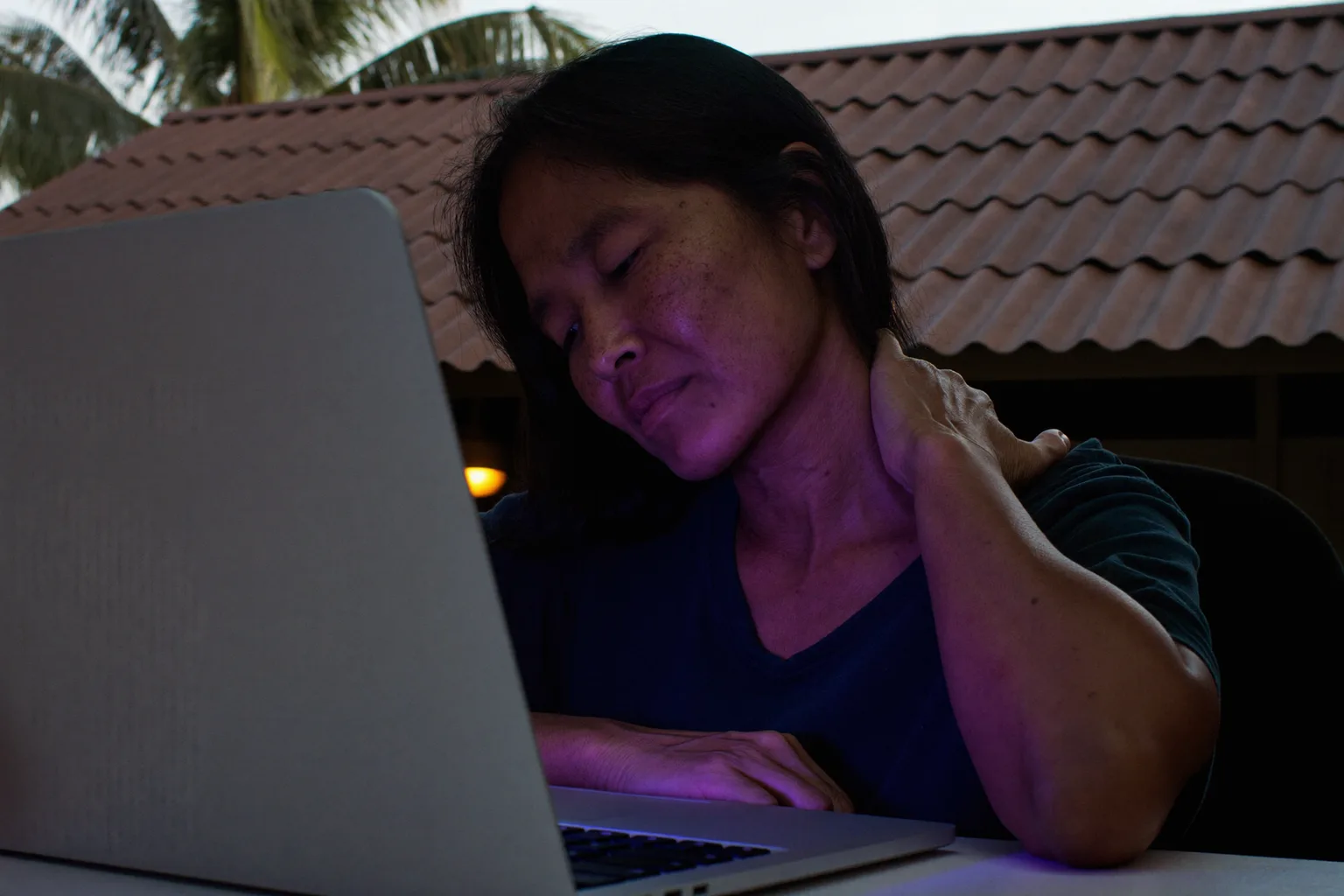 Isang tao sa desk na humahawak sa batok habang nasa harap ng laptop, ipinapakita ang matigas at masakit na leeg matapos ang mahabang araw sa computer