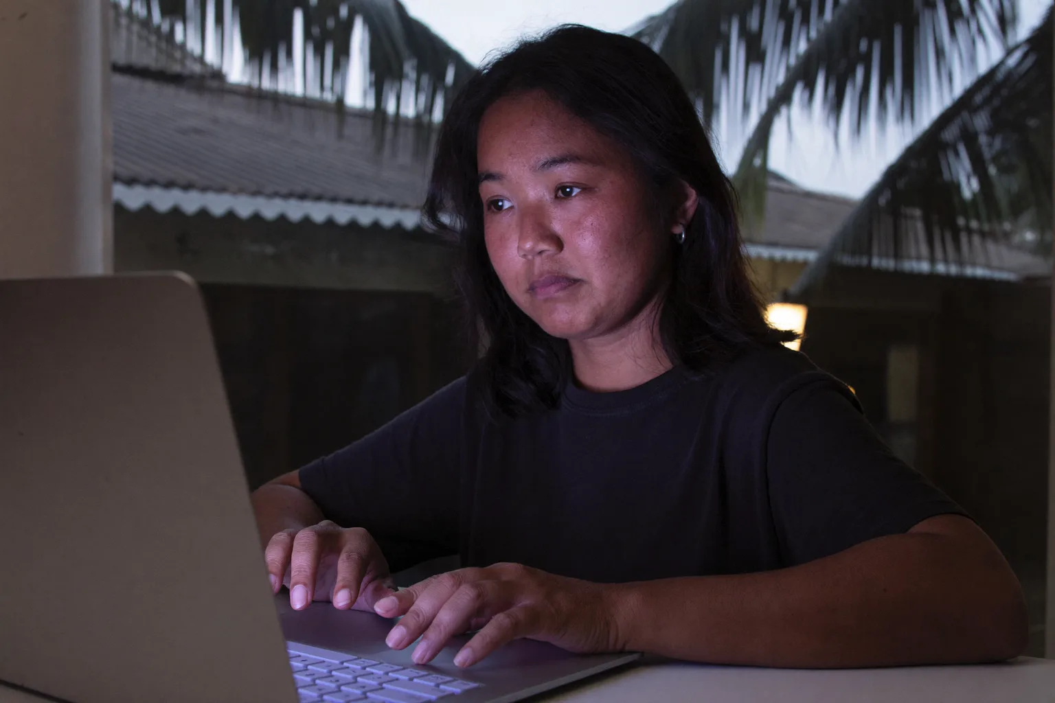Isang taong nakaupo sa home desk nang gabing-gabi na, nakatitig sa likod ng laptop screen habang nasa keyboard pa rin ang mga kamay, nagpapakita ng walang-buhay na pagod ng burnout sa trabaho