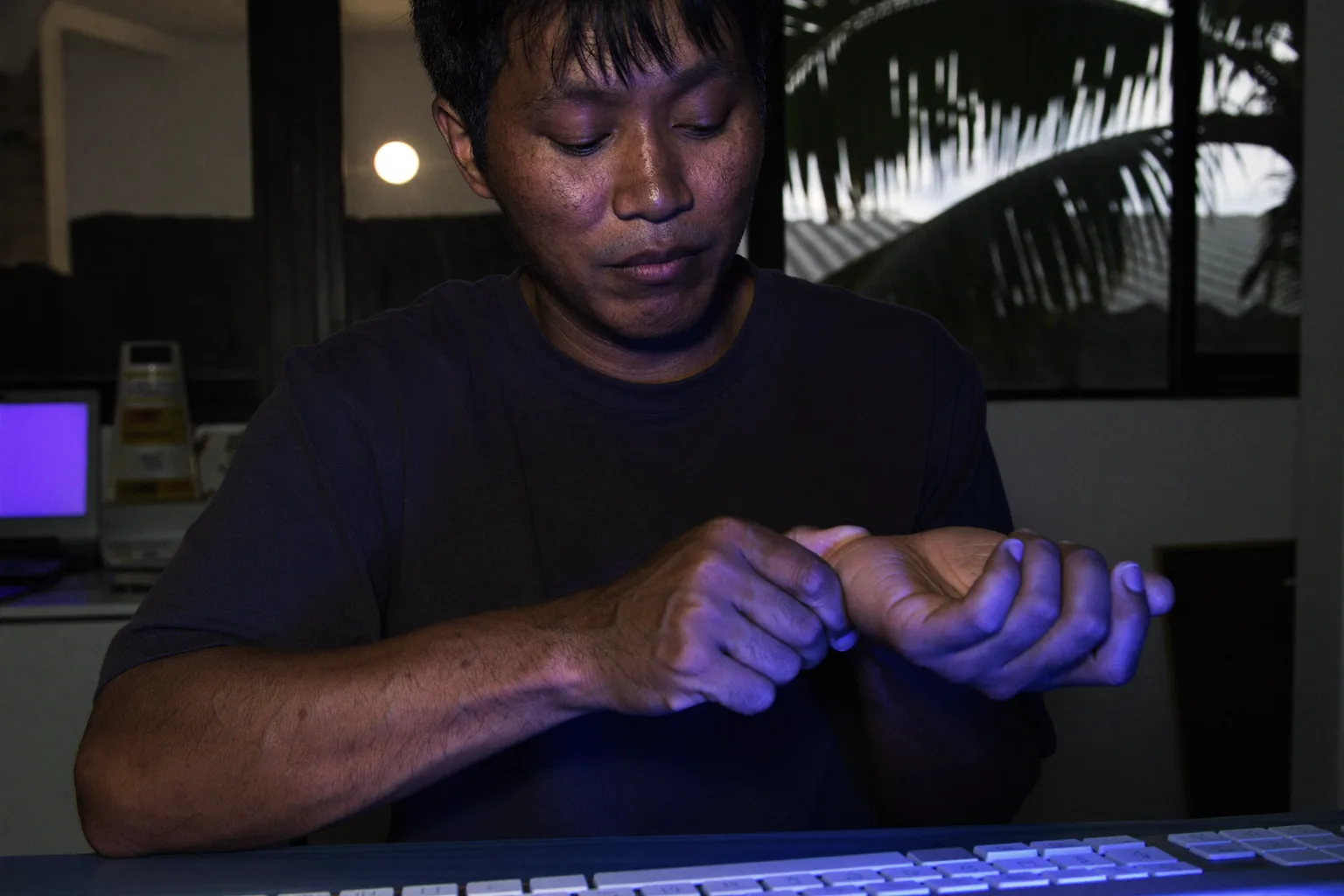 Isang taong nakaupo sa desk, hawak ng isang kamay ang kanang galang-galangan habang nasa harapan ang keyboard, na nagpapakita ng namamanhid at masakit na kamay dahil sa carpal tunnel