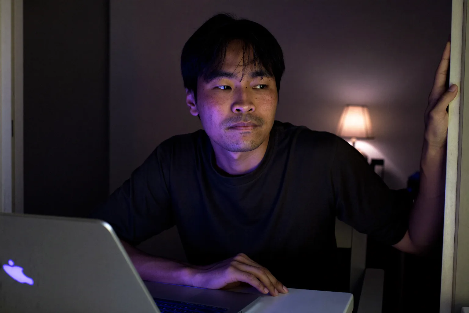 Nakasarang laptop sa home desk tuwing gabi na may bukas na ilaw sa kwarto at may taong naglalakad palayo, simbolo ng pagtatapos ng isang araw ng work from home