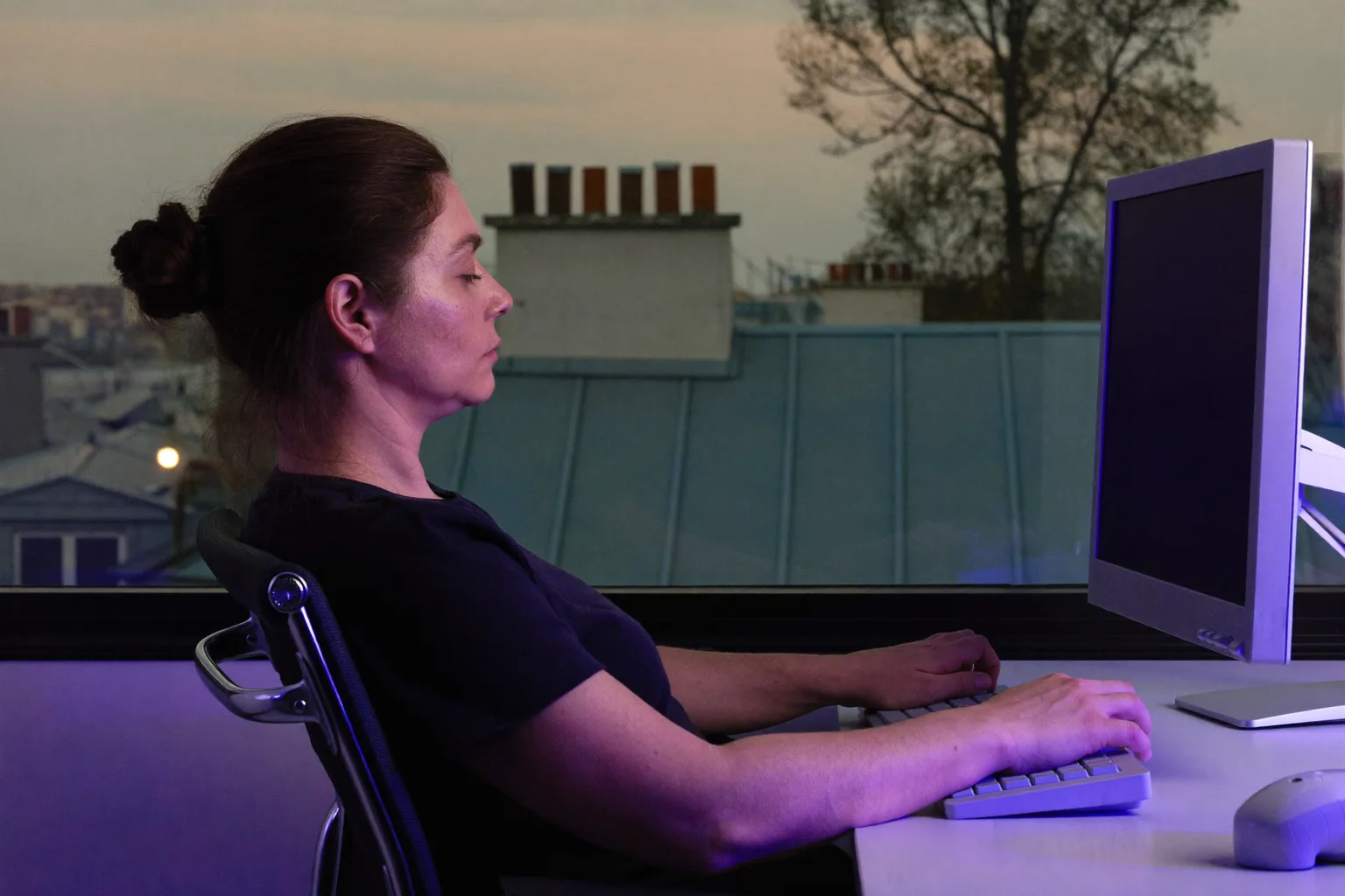 Une personne vue de profil, assise à un bureau, les pieds à plat au sol, le dos calé contre le dossier, les avant-bras à hauteur du bureau et l’écran au niveau des yeux : la posture de référence au bureau