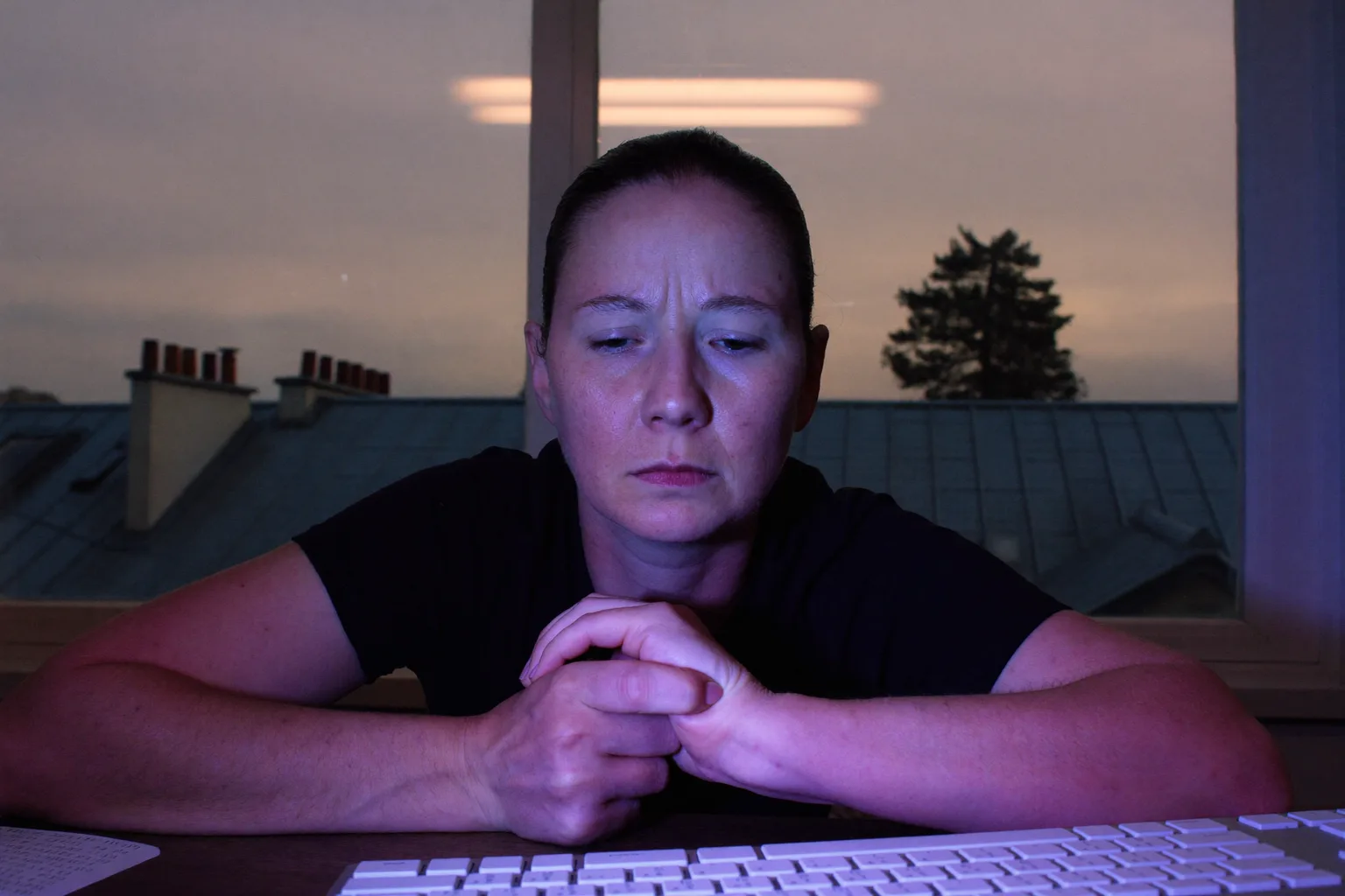 Une personne à son bureau tenant son poignet droit de l’autre main, clavier devant elle, illustrant la main engourdie et douloureuse des symptômes du canal carpien