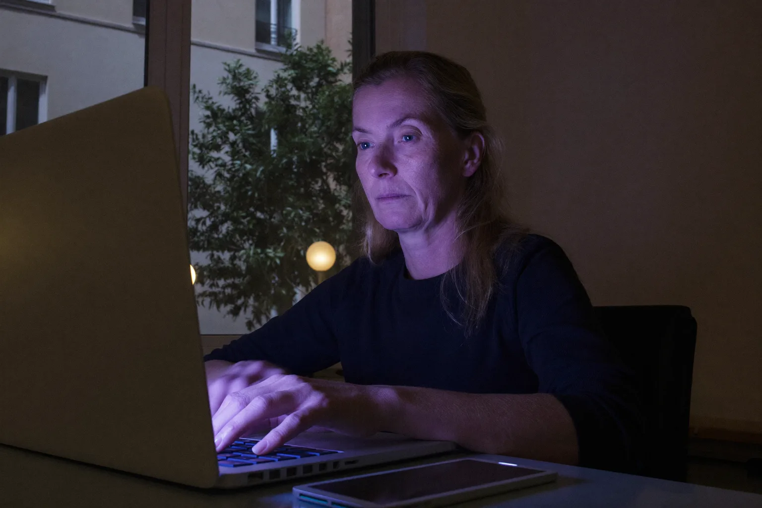 Egy ember késő este otthoni íróasztalánál ül, a laptop képernyője mögé mered, kezei még mindig a billentyűzeten, ami a munkahelyi kiégés kifejezéstelen kimerültségét mutatja