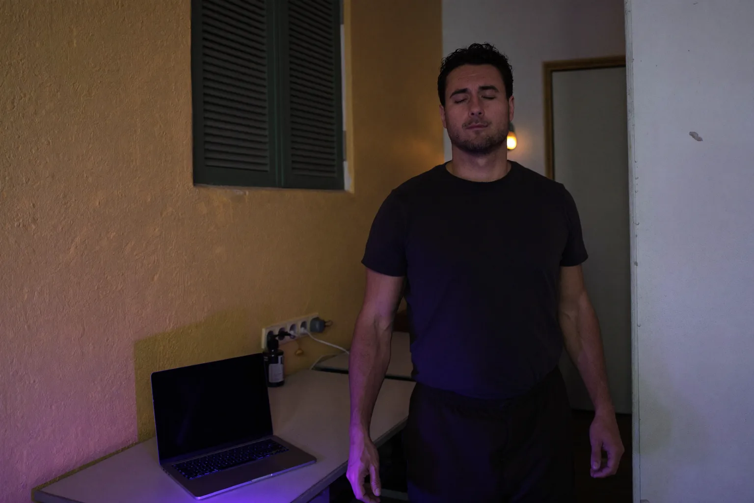 Un laptop chiuso su una scrivania di casa la sera, con la luce della stanza accesa e la persona che si allontana, a segnare la fine di una giornata di smart working