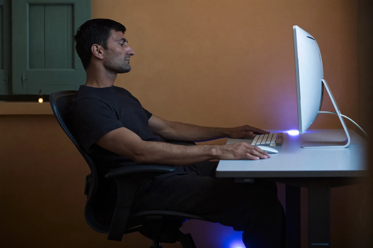 Una persona vista di profilo, seduta alla scrivania, con i piedi ben appoggiati al pavimento, la schiena contro lo schienale, gli avambracci all’altezza della scrivania e il monitor all’altezza degli occhi: la postura di riferimento alla scrivania