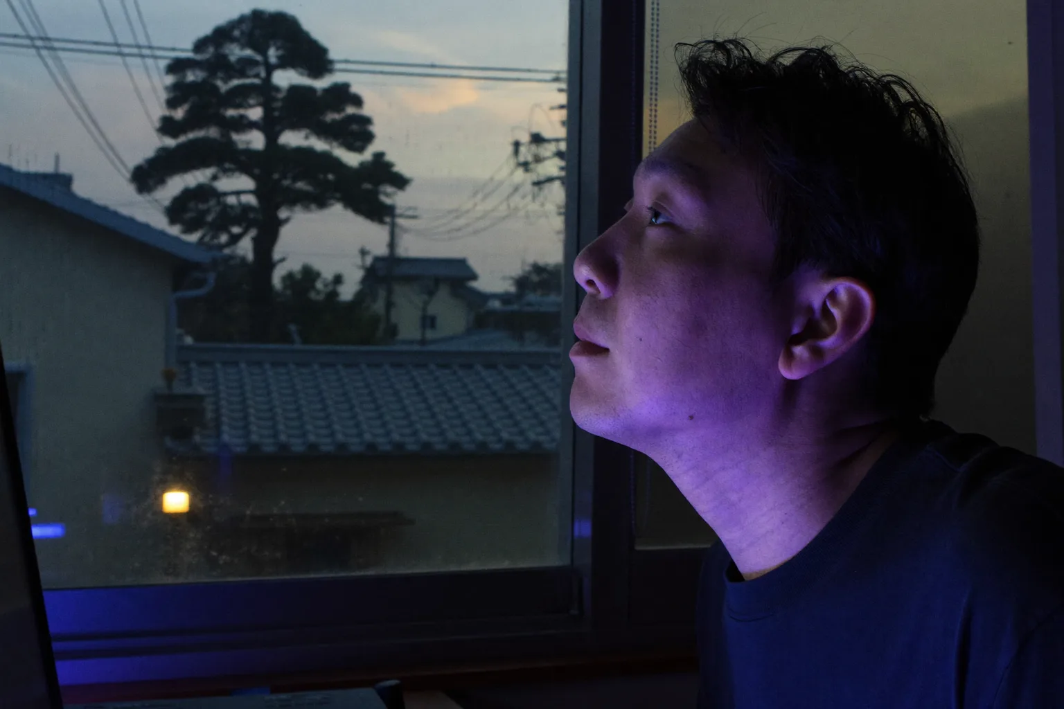 20-20-20ルールで眼精疲労を防ぐ様子:ノートパソコンから目を離し、窓の外の遠くの木を見ている人