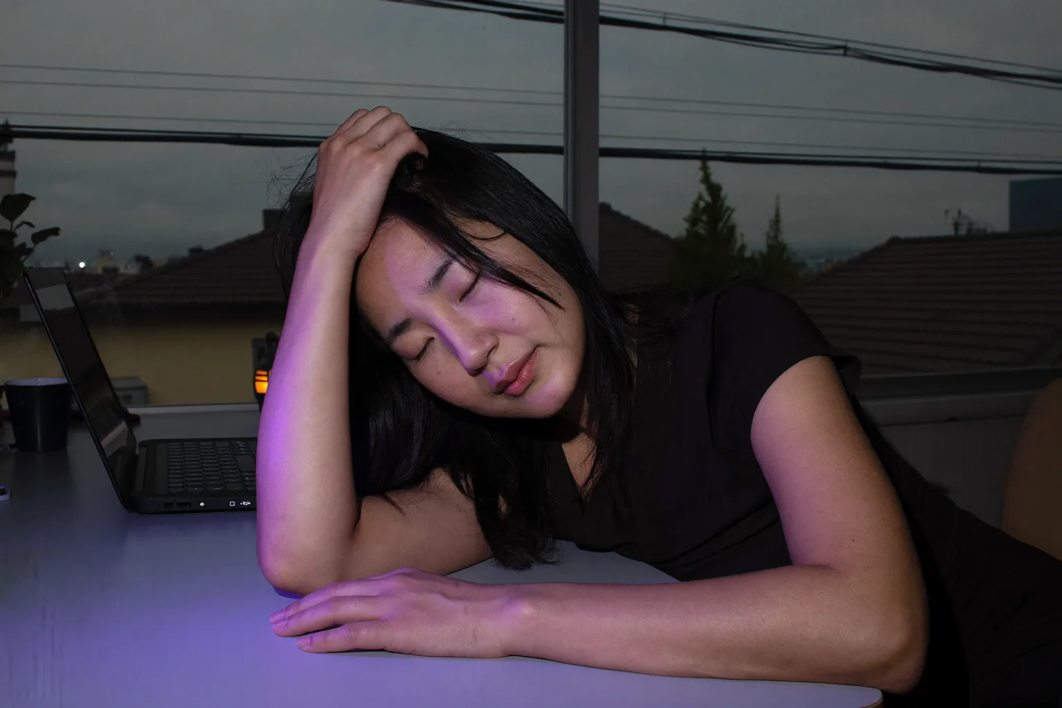 夜遅く、自宅の机に向かう人物。片手の指を髪に差し込むように頭を傾け、視線は伏せて焦点が合っておらず、もう一方の前腕は何もない机の上でじっと動かないままになっている