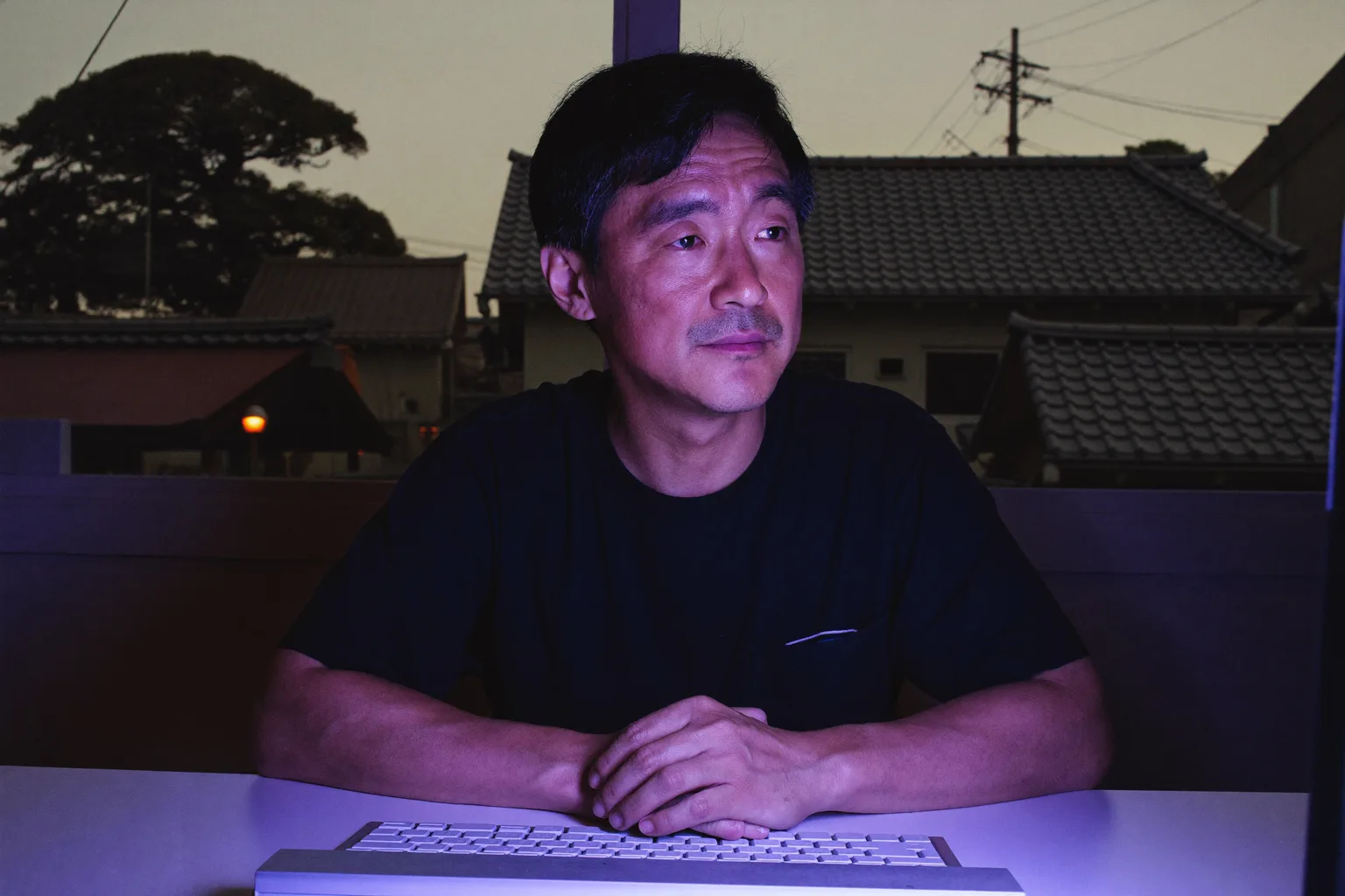 在宅勤務の夜遅く、自宅のデスクでノートパソコンの画面をぼんやりと見つめながら、指をキーボードに置いたまま固まっている人。仕事による燃え尽き症候群特有の、感情の平坦さを表している