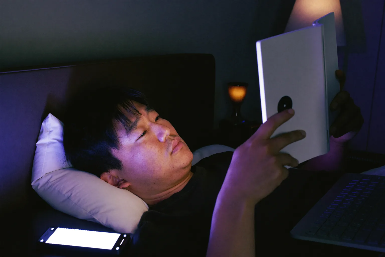 늦은 밤 침대에서 전자책 리더기를 읽는 남자. 화면은 얼굴에 겨우 닿을 만큼 희미한 빛만 낸다. 반면 옆 협탁 위에 놓인 스마트폰은 화면을 위로 향한 채 두 번째 램프갓을 딱딱하고 차가운 블루라이트로 가득 채운다