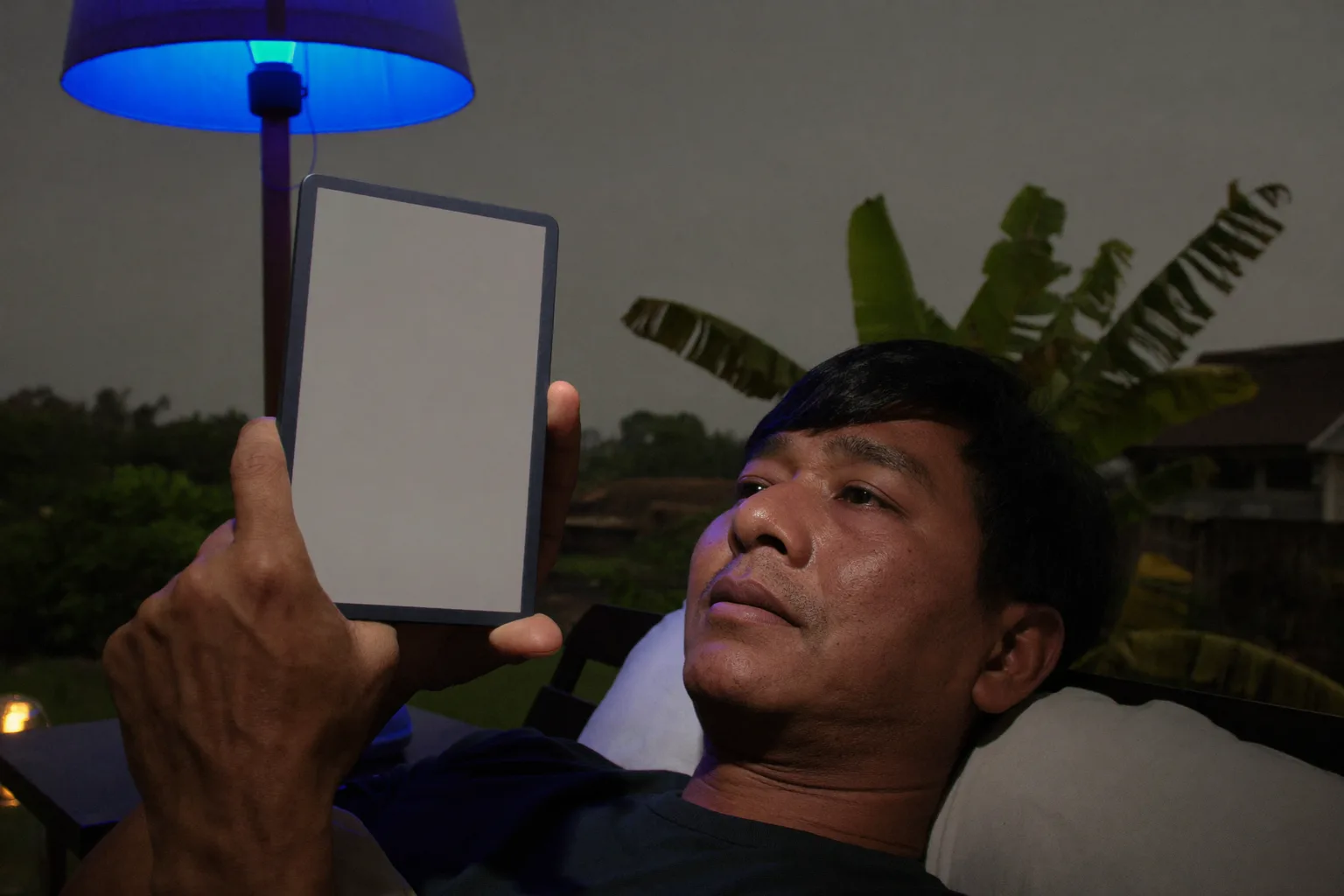 Seorang lelaki membaca e-pembaca di atas katil lewat malam, halamannya bercahaya malap yang hampir tidak sampai ke wajahnya, manakala di atas meja sisi sebelahnya sebuah telefon terbaring menghadap atas membanjiri hujung bilik dengan cahaya biru sejuk yang terang