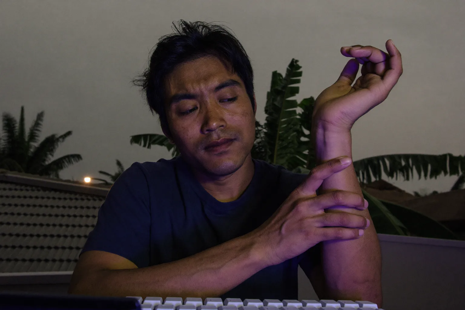 Seseorang di meja kerja memegang pergelangan tangan kanan dengan tangan sebelah lagi, papan kekunci di hadapannya, menggambarkan tangan yang kebas dan sakit akibat gejala sindrom terowong karpal