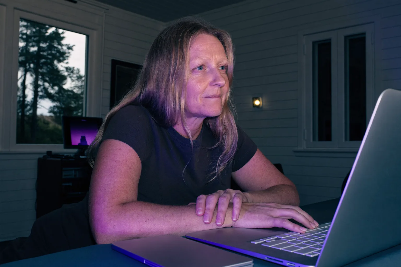 En person som sitter ved et hjemmekontor sent på kvelden, og stirrer forbi laptop-skjermen med hendene fortsatt på tastaturet, et bilde på den flate utmattelsen ved utbrenthet på jobb