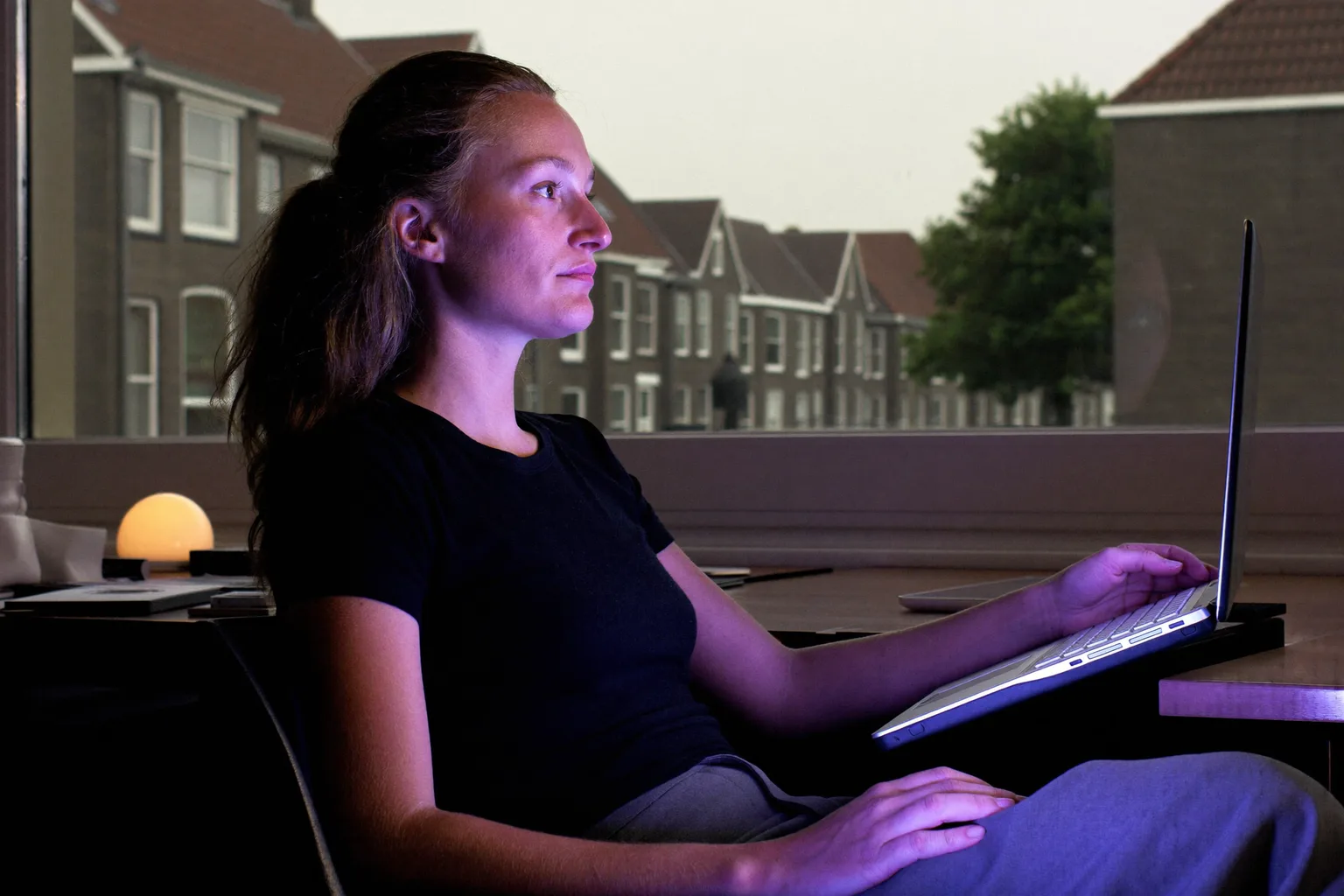 Kantoormedewerker past de 20-20-20-regel toe tegen oogvermoeidheid: blik weg van de laptop, het raam uit, naar een boom in de verte