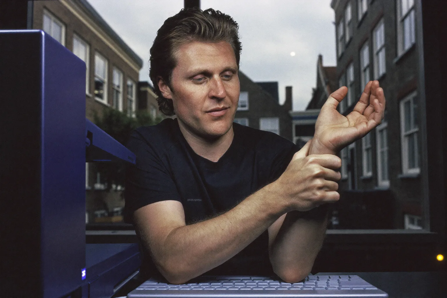 Iemand aan een bureau die met de ene hand de rechterpols vasthoudt, toetsenbord ervoor, de dove, pijnlijke hand van carpaaltunnelsyndroom in beeld