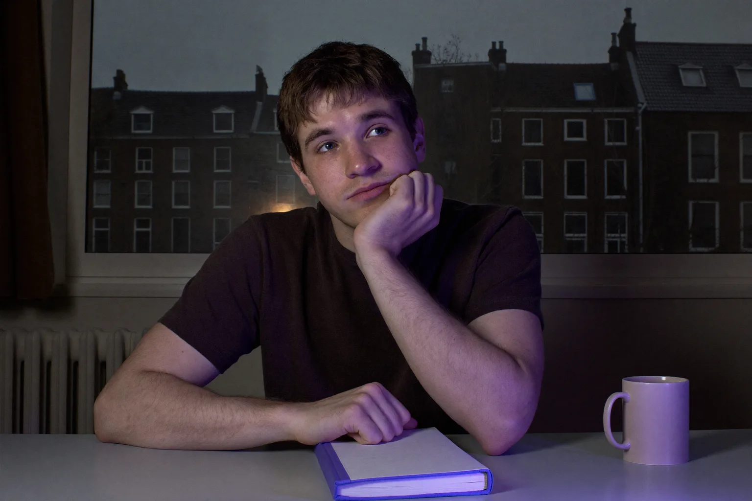 Een student laat op de avond aan een bureau, kin rustend in een open handpalm, gezicht van opzij verlicht door het schermlicht, blik afgedwaald van het werk en uit beeld