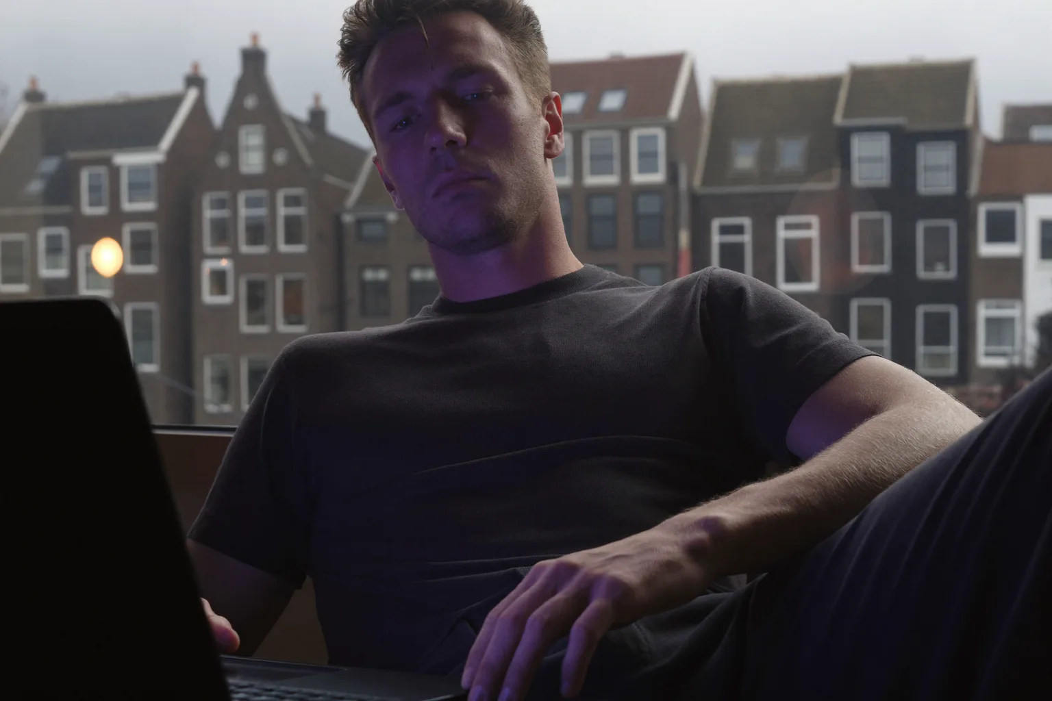 Een thuiswerker die aan zijn bureau even pauzeert om uit het raam te kijken, weg van de laptop
