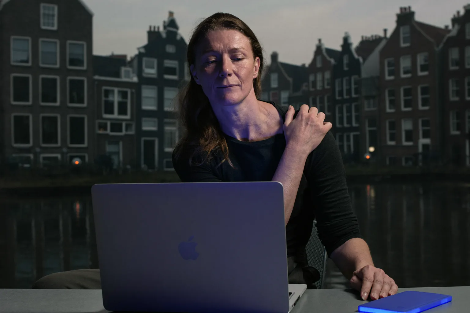 Iemand aan een bureau die met de hand naar achteren grijpt om de nek te masseren, voor een laptop, met de stijve, pijnlijke nek van een lange dag achter de computer
