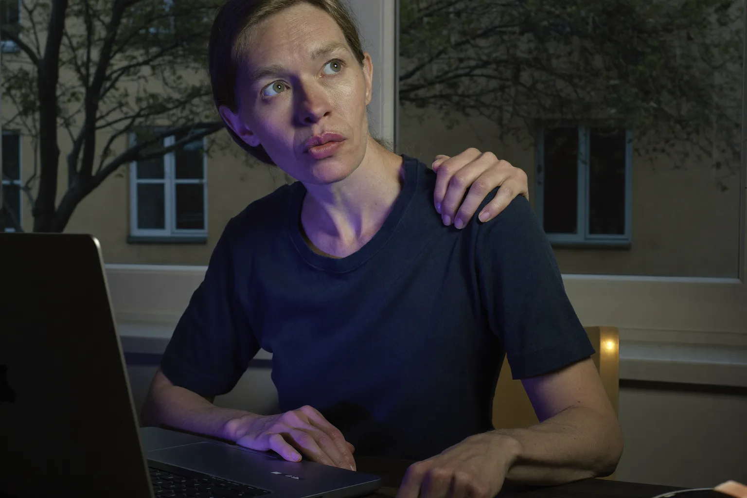 Osoba przy biurku sięgająca ręką za głowę, by rozmasować kark przed laptopem: obraz sztywnego, obolałego karku po długim dniu przy komputerze