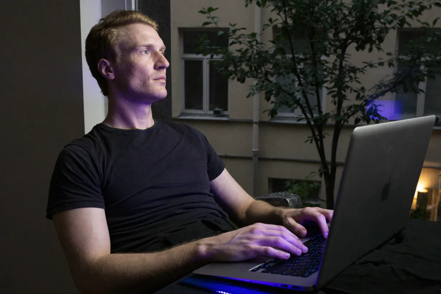 Osoba pracująca zdalnie robi przerwę przy domowym biurku i patrzy przez okno, z dala od laptopa