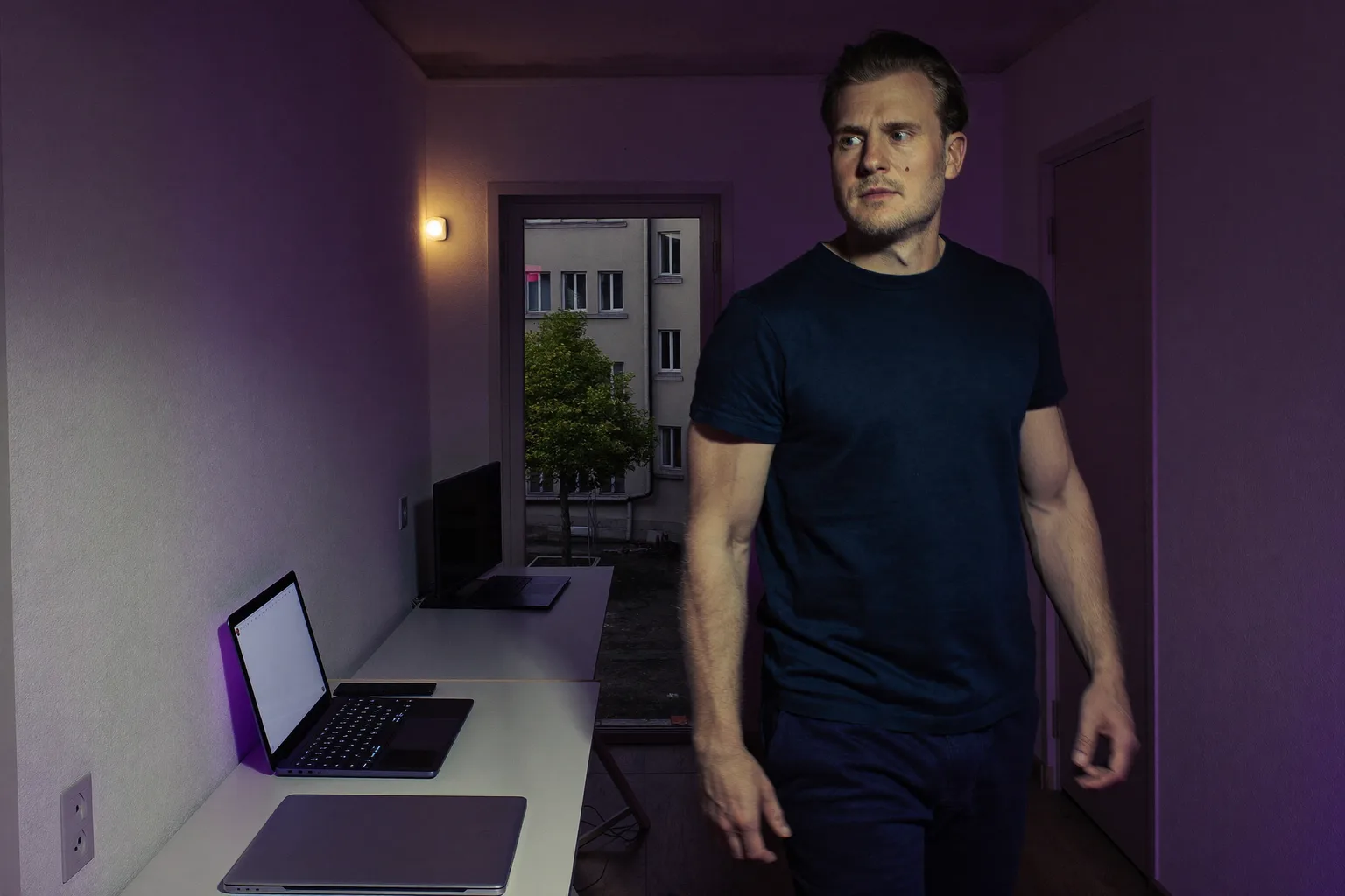 Zamknięty laptop na domowym biurku wieczorem, w pokoju pali się światło, a osoba odchodzi, co pokazuje koniec dnia pracy zdalnej