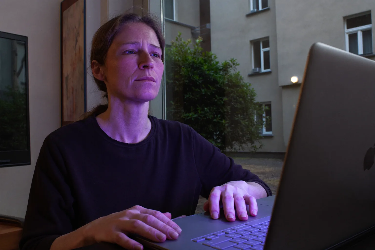 Osoba siedząca przy domowym biurku późnym wieczorem, wpatrująca się w pustkę ponad ekranem laptopa z dłońmi wciąż na klawiaturze, obraz płaskiego wyczerpania charakterystycznego dla wypalenia zawodowego