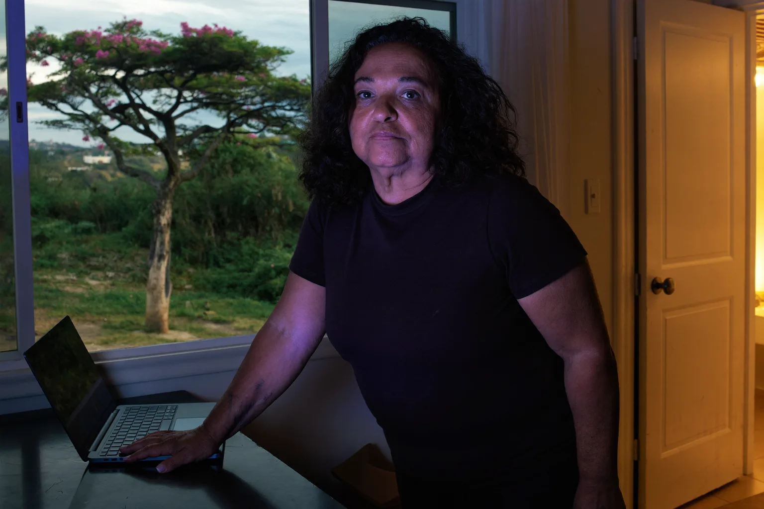 Um notebook fechado em uma escrivaninha em casa à noite, com a luz do quarto acesa e a pessoa se afastando, mostrando o fim de um expediente em home office