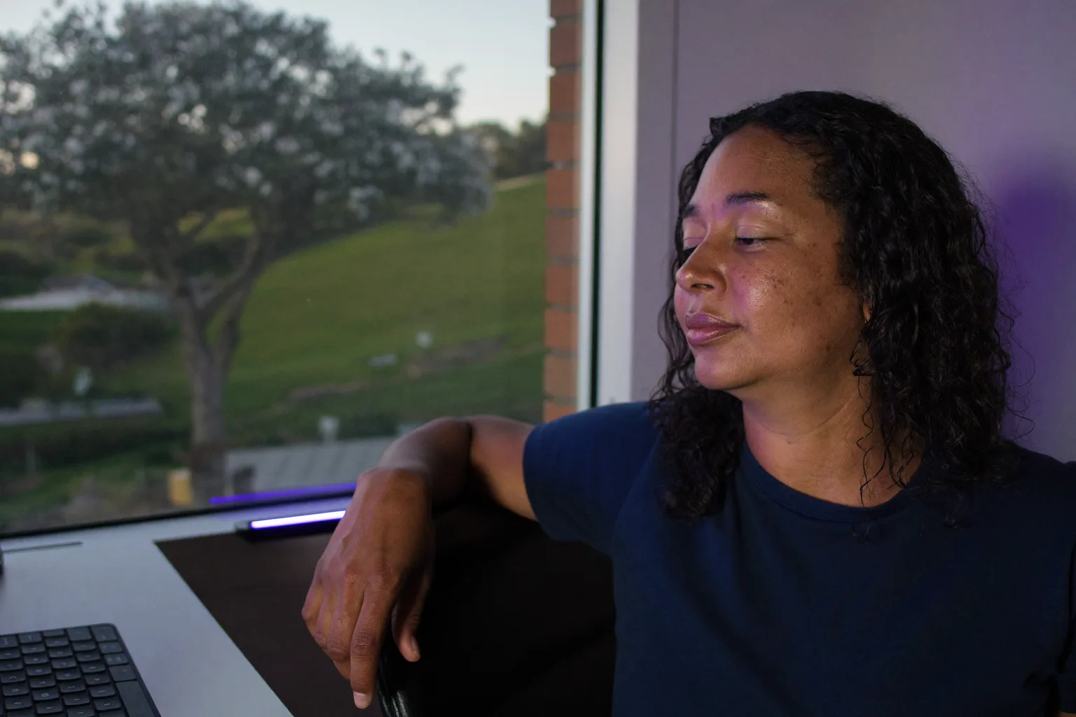Uma pessoa trabalhando em home office faz uma pausa na mesa de casa para olhar pela janela, longe do notebook