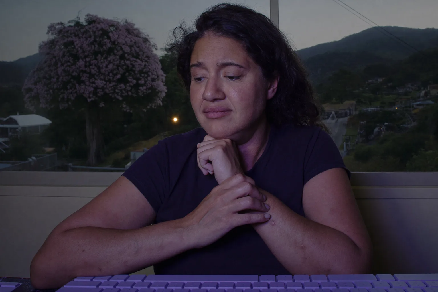 Uma pessoa sentada à mesa segurando o próprio pulso direito com a outra mão, teclado à frente, mostrando a mão dolorida e dormente dos sintomas de túnel do carpo