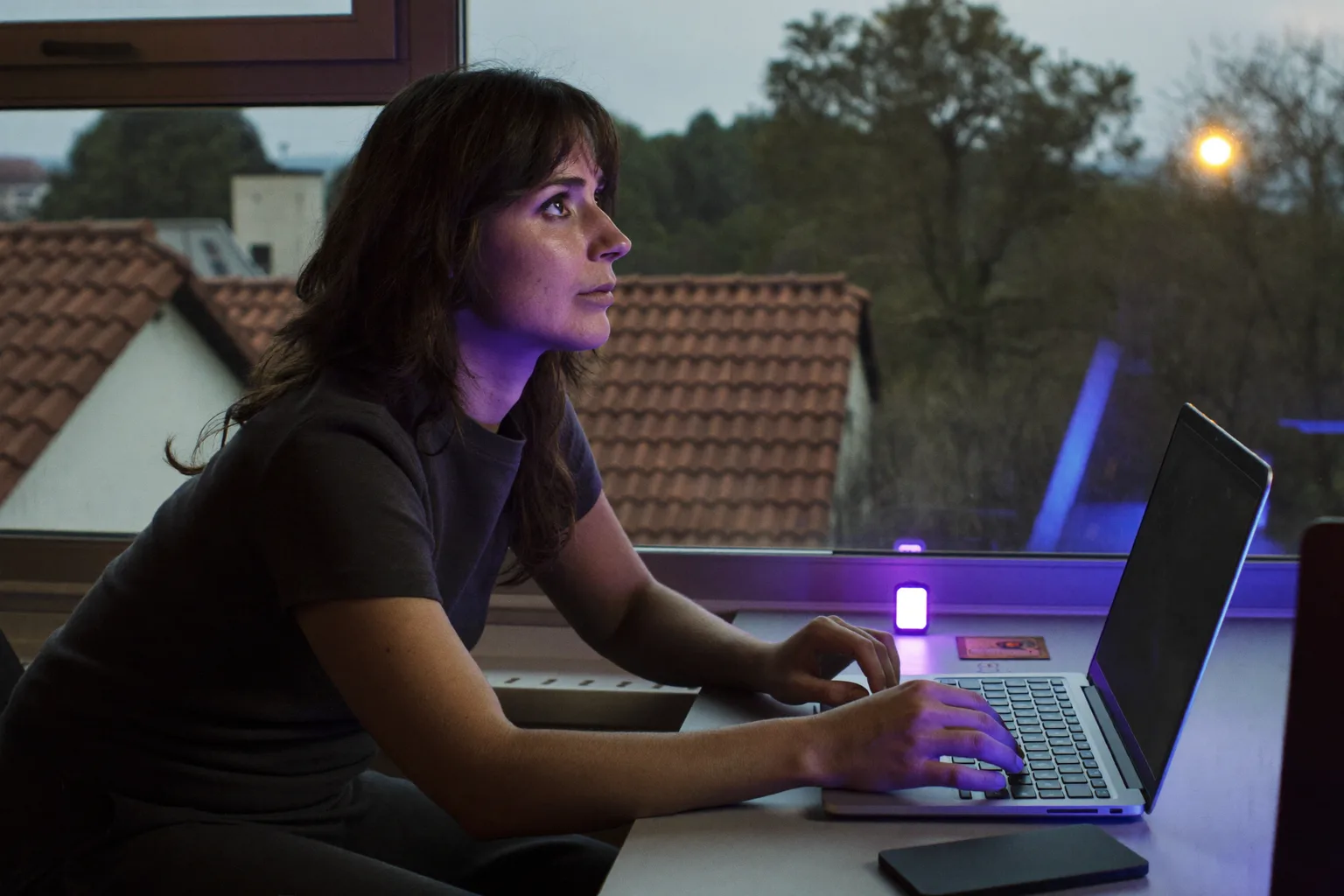Persoană care lucrează la ecran și aplică regula 20-20-20 împotriva oboselii oculare, privind departe de laptop, pe fereastră, către un copac aflat la distanță