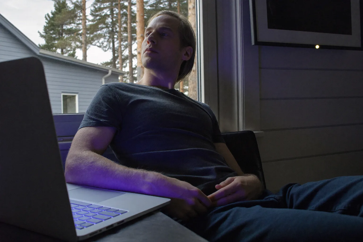 En person som jobbar hemifrån tar en paus vid skrivbordet för att titta ut genom fönstret, bort från laptopen