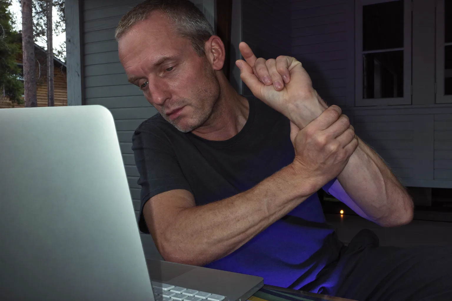 En person vid ett skrivbord som håller sin högra handled med andra handen, tangentbord framför sig, och som visar den domnade, värkande handen vid karpaltunnelsyndrom