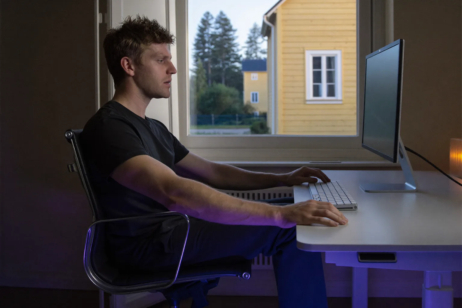 En person sedd från sidan som sitter vid ett skrivbord med fötterna platt mot golvet, ryggen mot stolens stöd, underarmarna i nivå med skrivbordet och skärmen i ögonhöjd: referenshållningen vid skrivbordet
